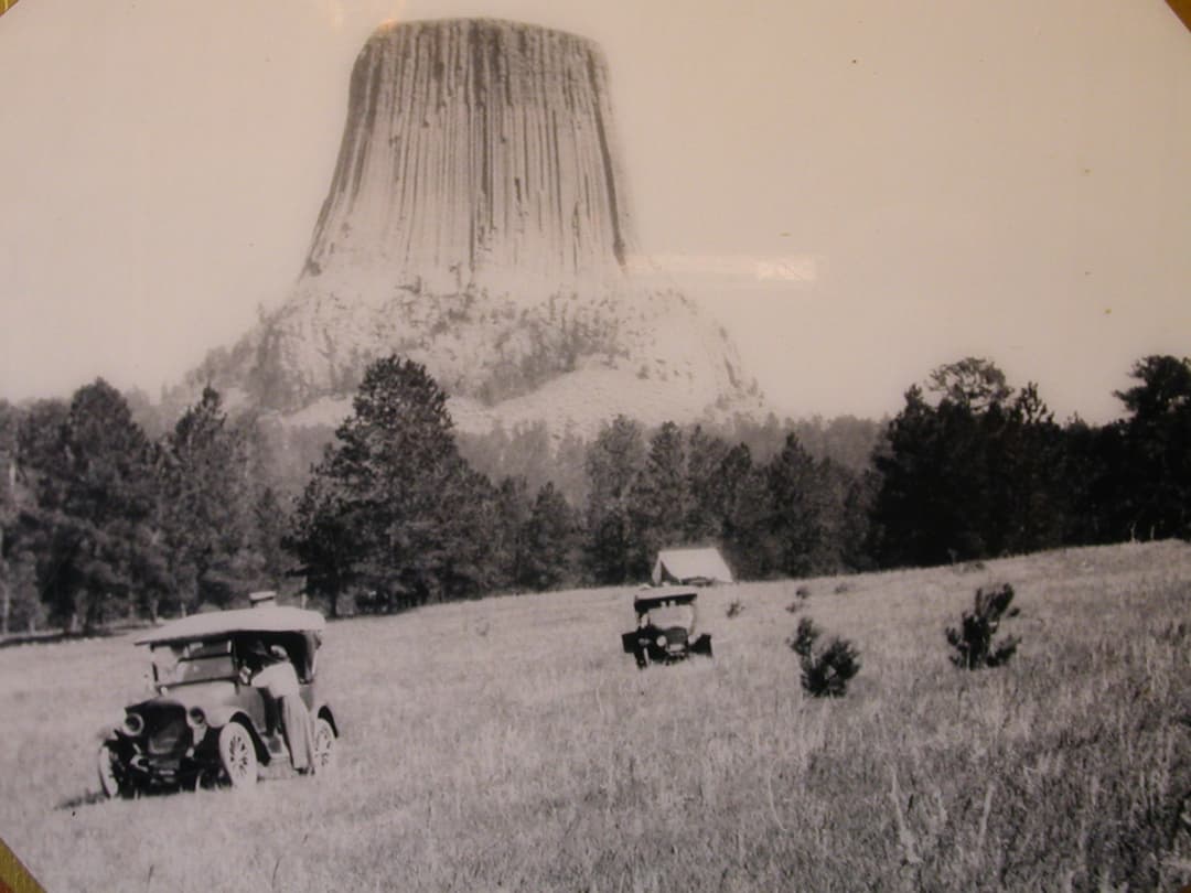 Historic view of early automobiles in the meadow below Devils Tower