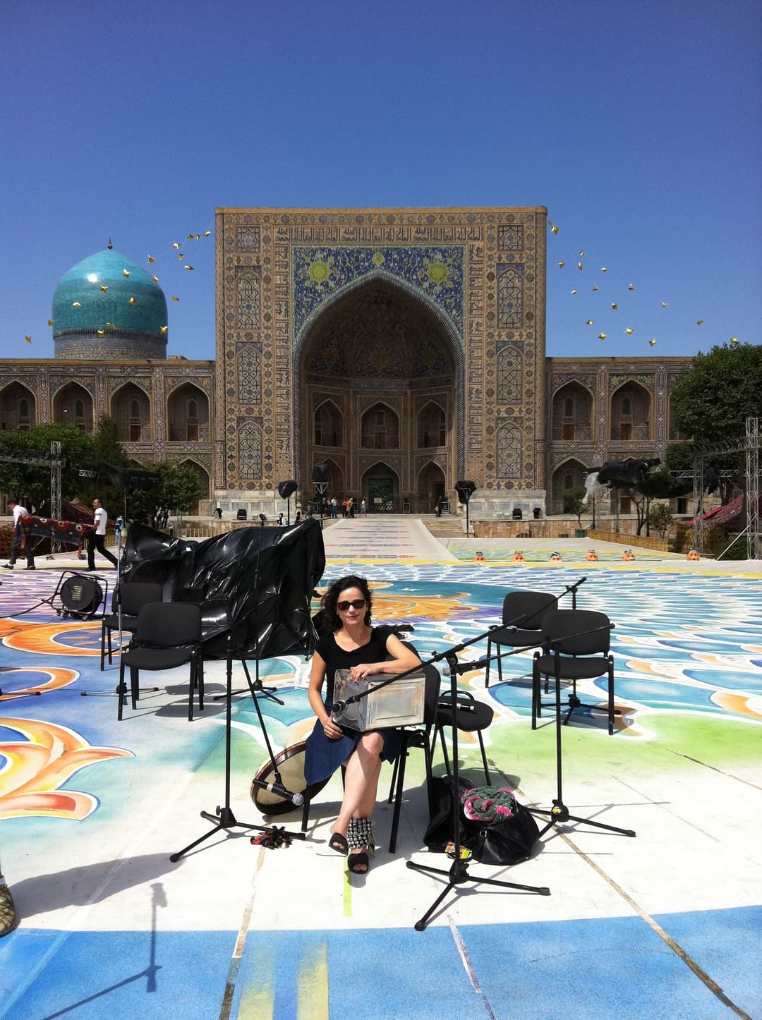 A musician seated on stage before Tilya-Kori Madrasah and its turquoise dome.