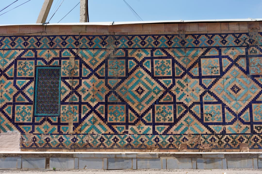 Geometric glazed tile mosaic and screened window on exterior wall