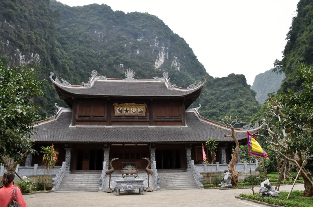 Front view of a traditional wooden temple hall backed by limestone mountains.