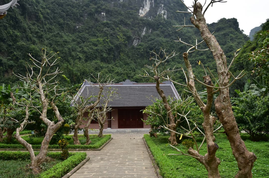Stone path leading to a traditional hall against a steep limestone mountain.