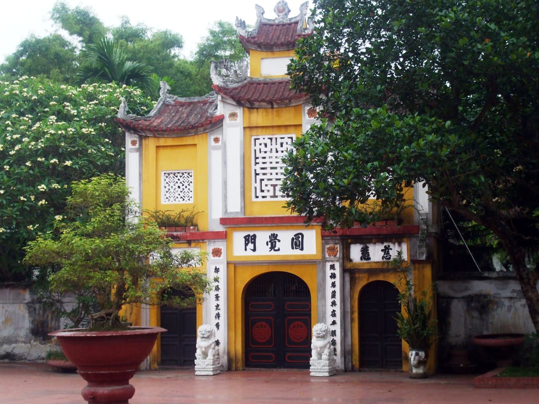 Front entrance gate of Trần Quốc Pagoda flanked by stone lions and bonsai.