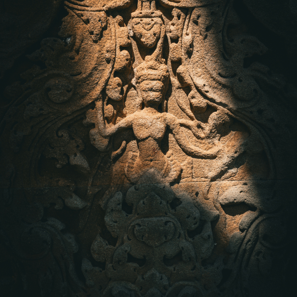 A cross-legged figure with their palms reaching upward. Shadow is covering most of the wall engraving.