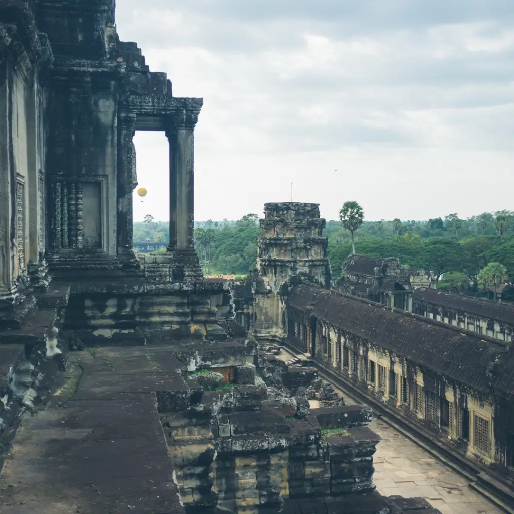 Un balcón exterior del templo de Angkor Wat. Se ven las copas de los árboles al fondo con un cielo nublado.