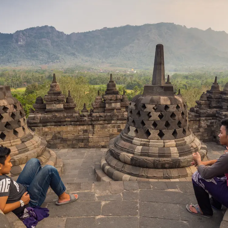 两名男子坐在婆罗浮屠寺的塔顶，周围是佛塔。