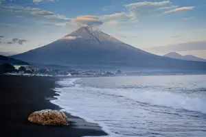 يمكن رؤية جبل أغونغ في المسافة خلف الأمواج الرغوية لشاطئ في المقدمة.