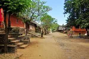 شارع ترابي مع مباني حمراء ودرجات وأشجار على جانبيه في Tenganan Pegringsingan.