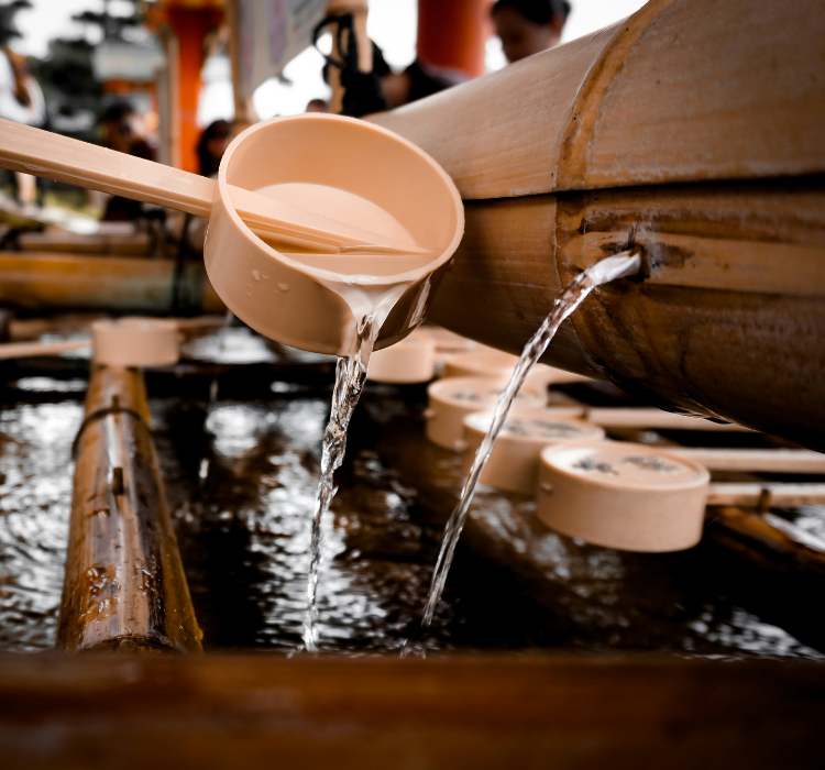 A pink-tan ladel pouring water into a basin at the base of the chozuya near the Fushimi Inari Taisha Shrine Temple in Kyoto, Japan.