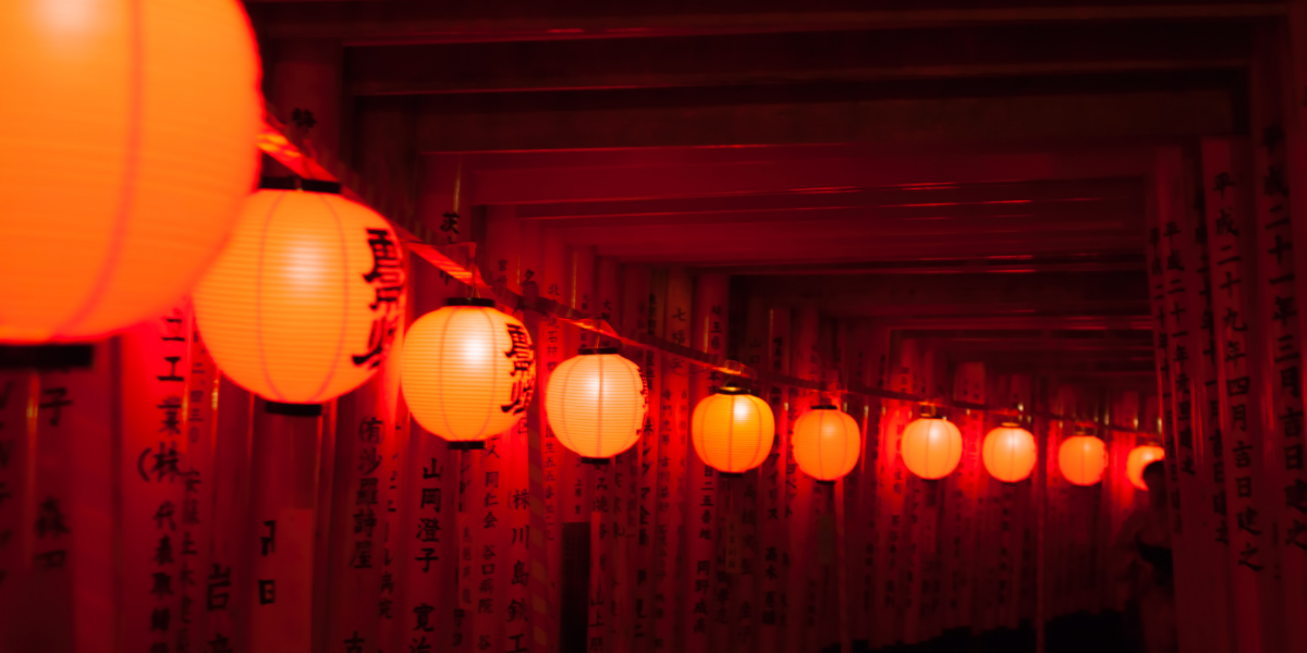 A string of red circular paper lanterns illuminated beneath Torii gates at the Fushimi Inari Taisha Shrine Temple.