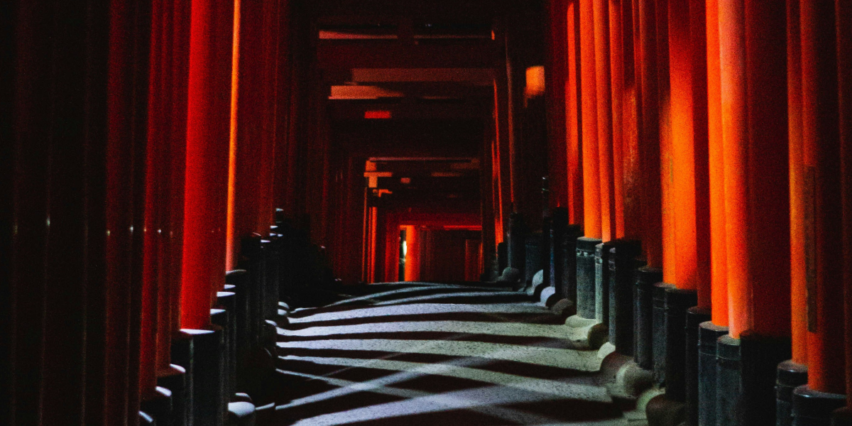 The Torii Gates of the Fushimi Inarju Taisha Shrine Temple at night. Columns of light from spotlights from outside the series of Torii gates form an interesting crossed pattern on the stone path beneath the Torii gates of varying brilliance and width.