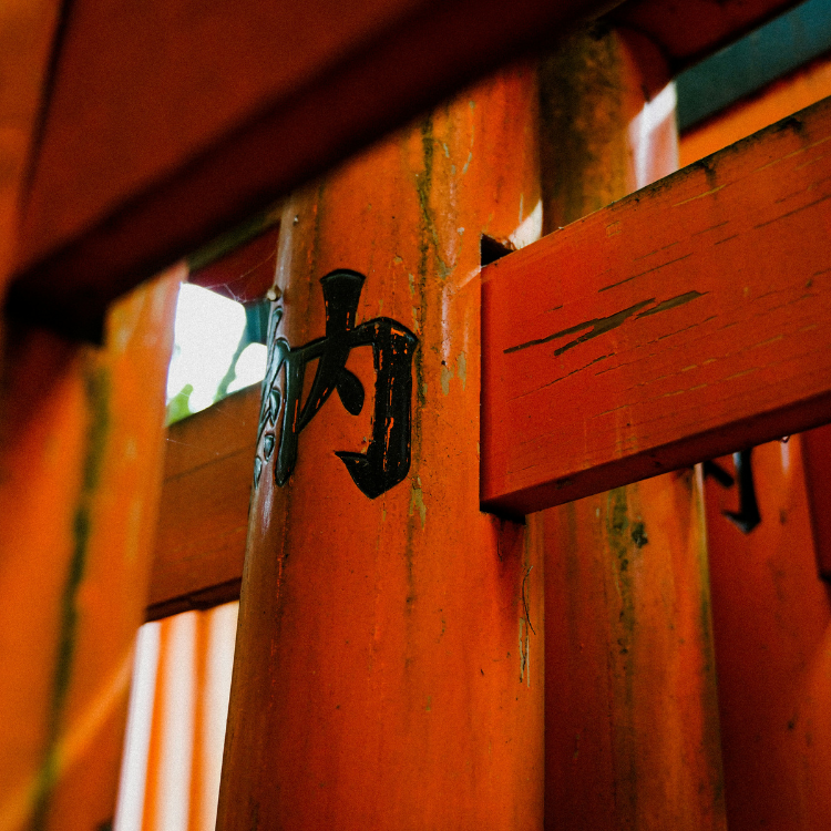 A black, painted symbol on a red wood torii gate at the Fushimi Inari Taisha Temple.