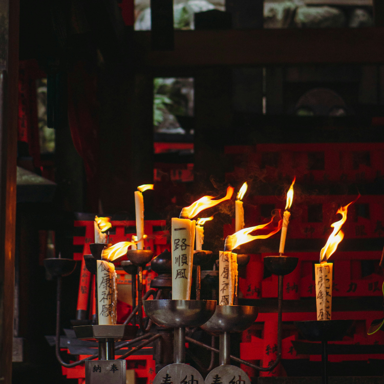 Ten candles that are tan and the black symbols burning in a dark room.